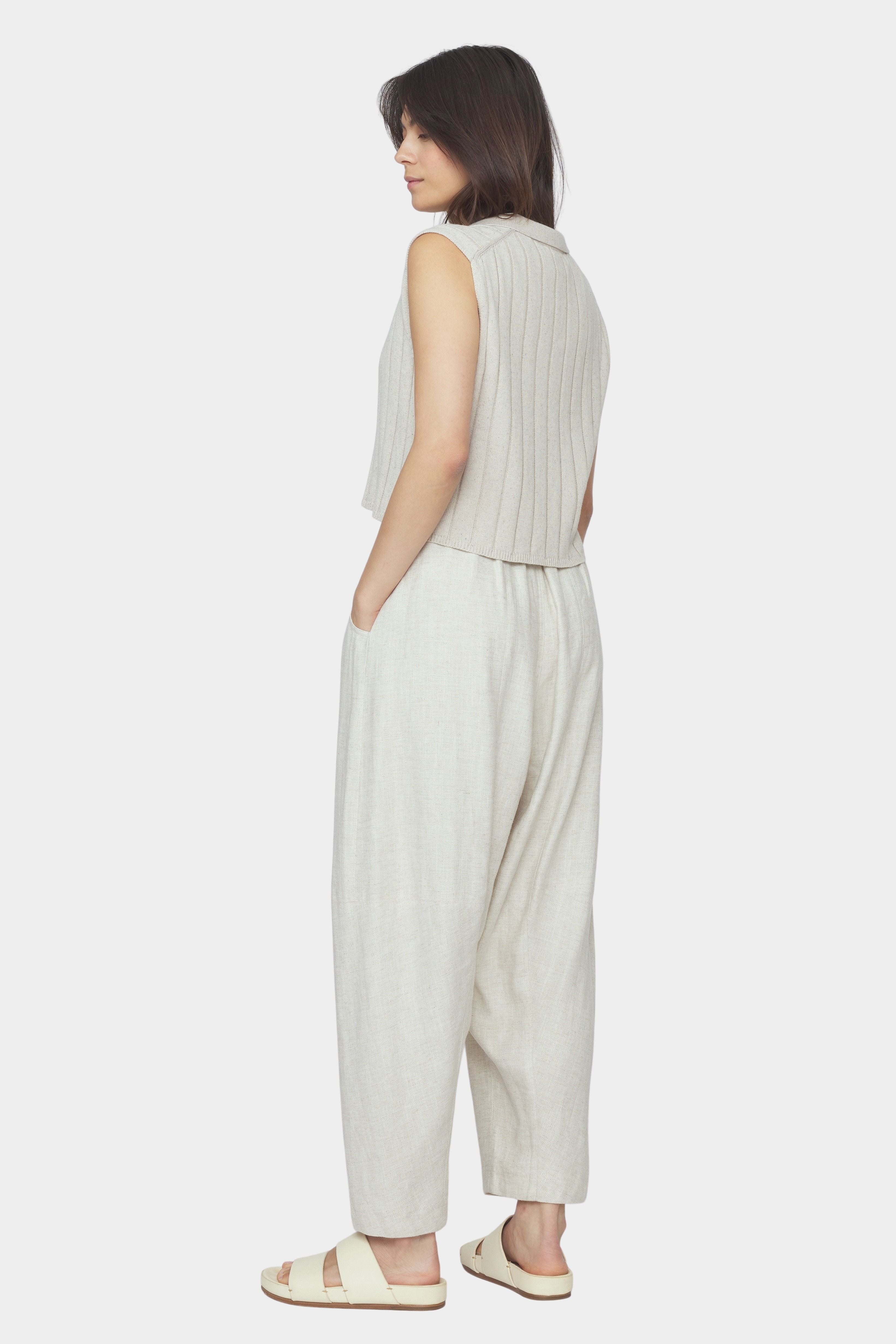 Back and side view of speckle beige sleeveless ribbed knit vest with collar and cropped hem styled with relaxed light beige pants