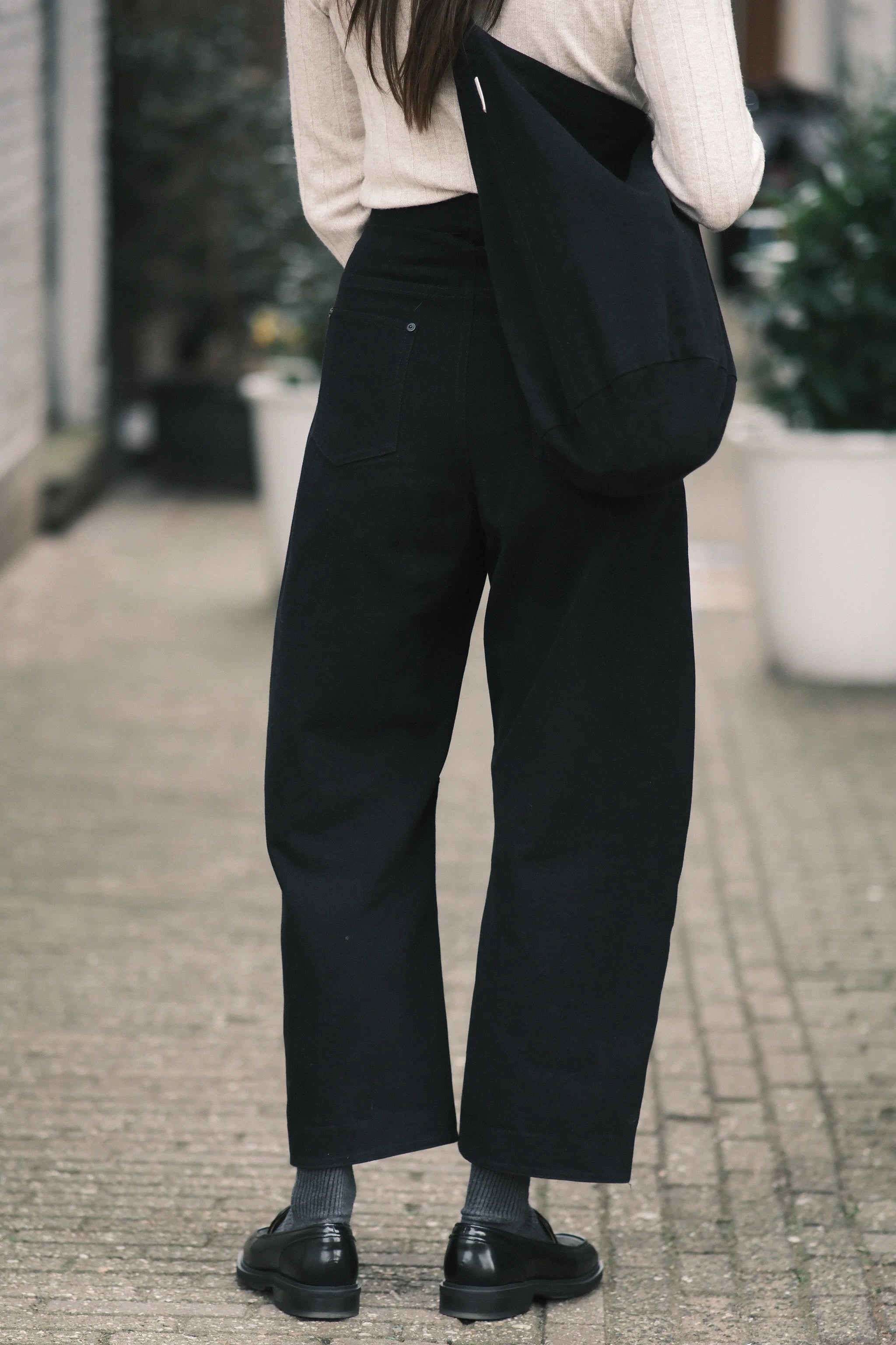 Back view of the black curved leg trouser showing a patch pocket and the tapered hem