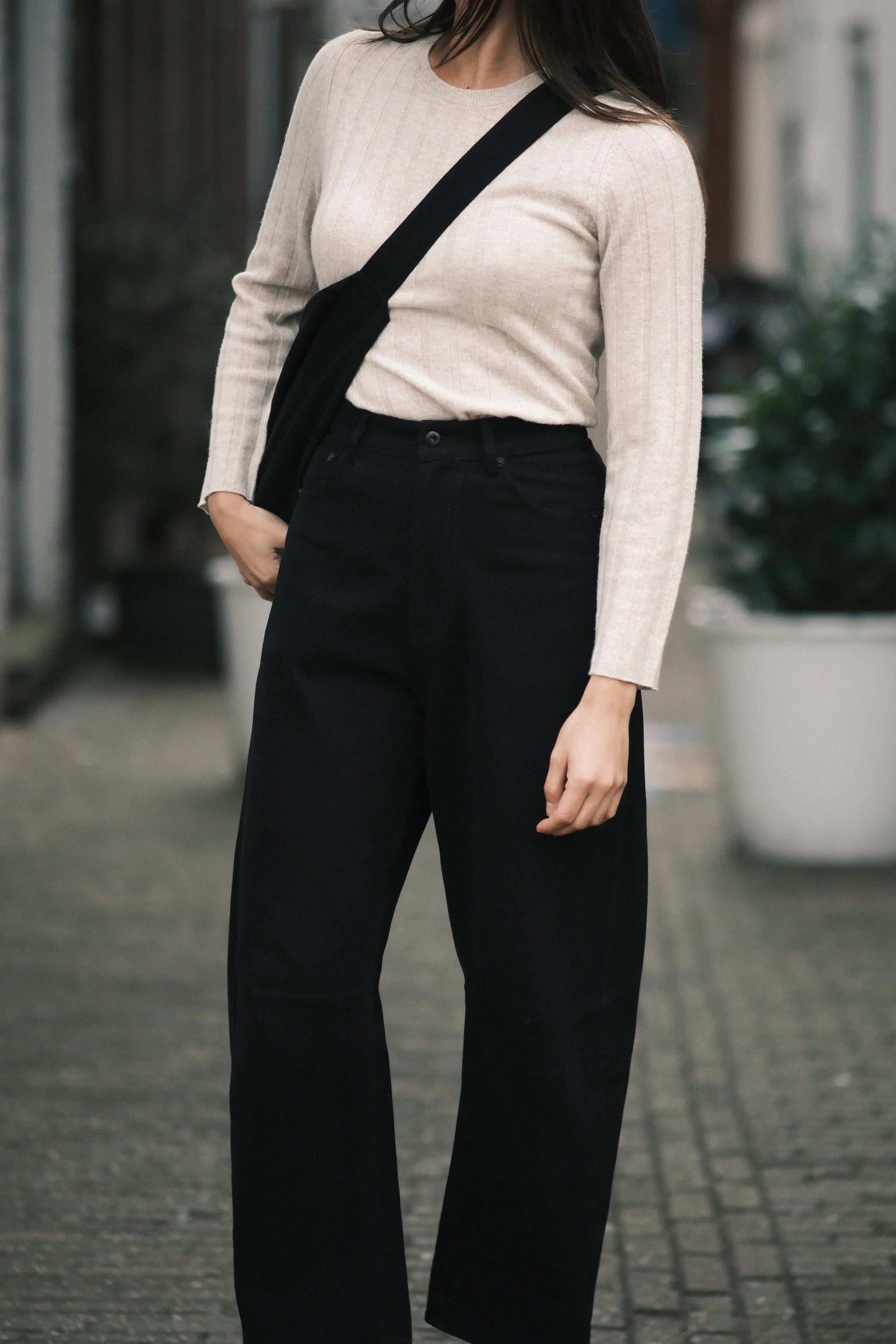 Full front view of the black curved leg work trouser styled with a cream ribbed knit and crossbody bag