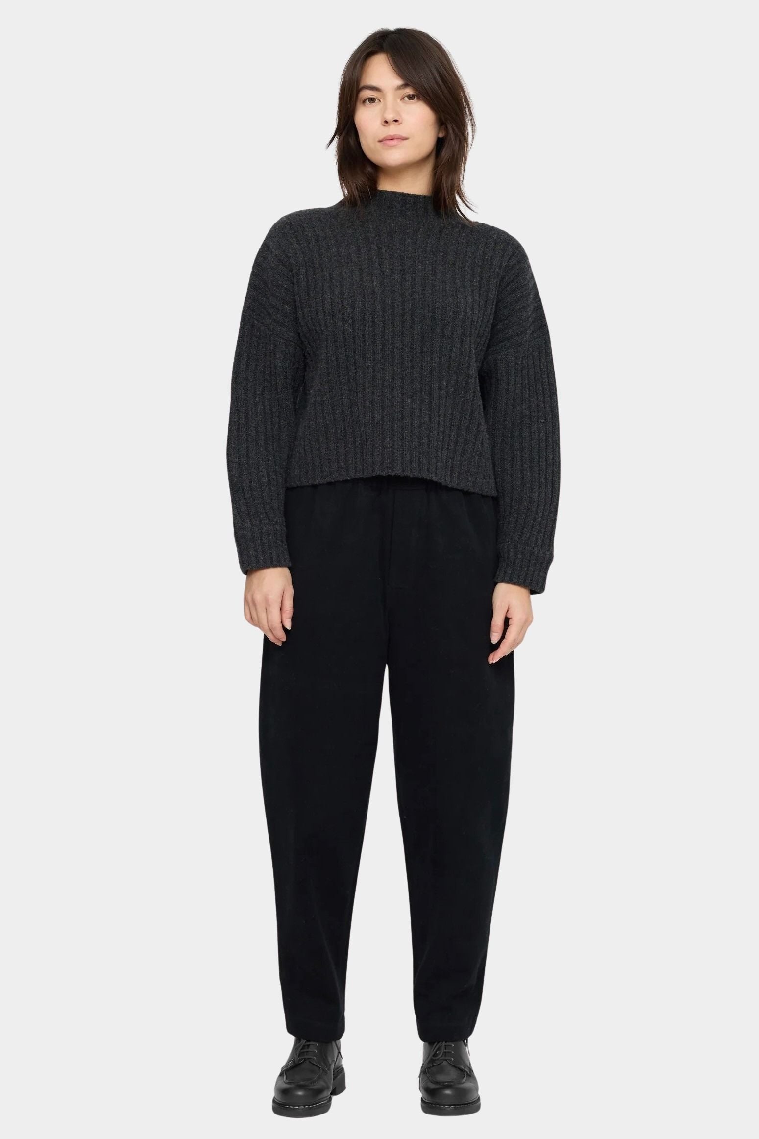 Model wearing the black elastic waist trouser with a charcoal ribbed sweater and black lace-up shoes