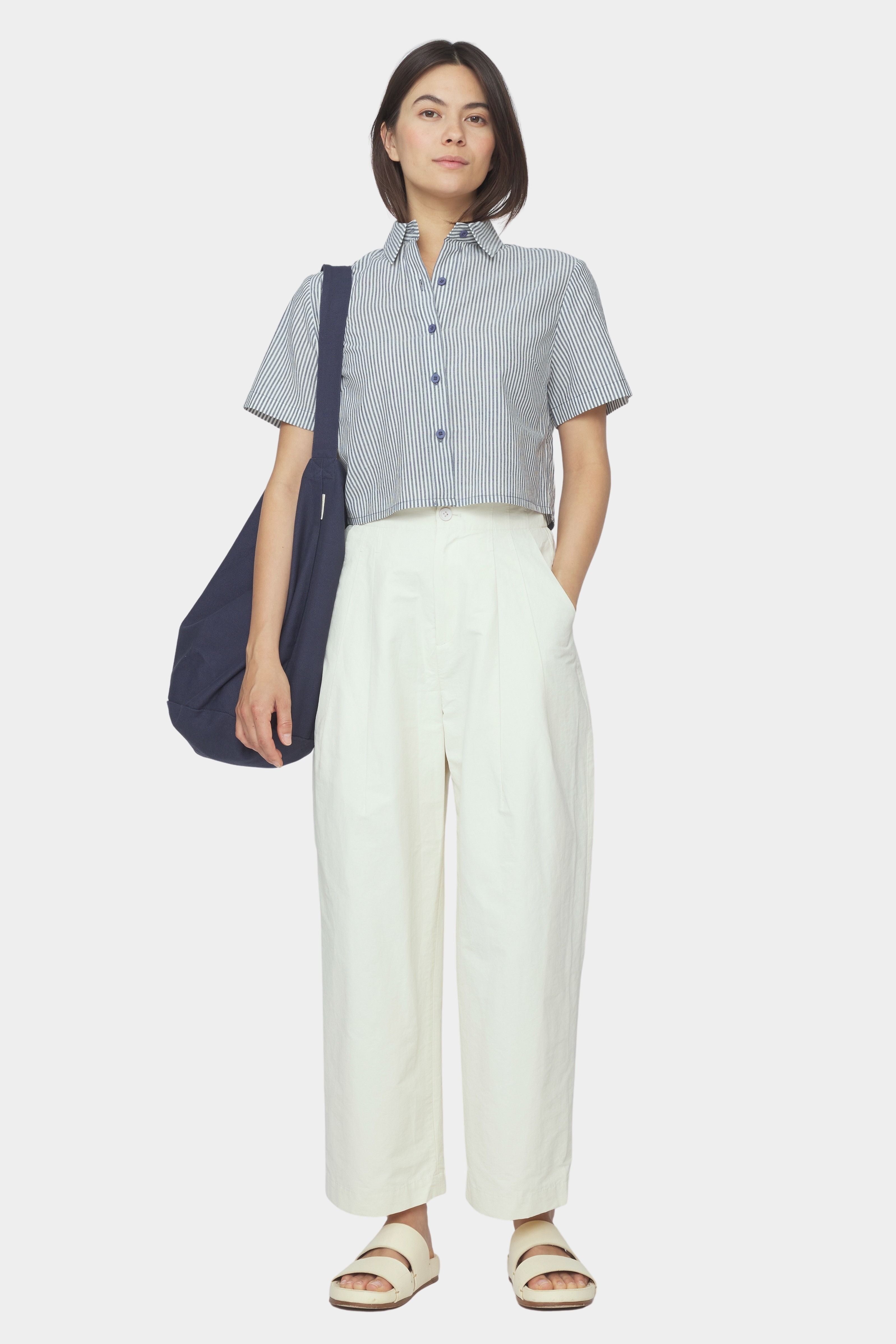 Front view of navy striped cropped shirt with short sleeves and button front styled with ivory trousers and a navy shoulder bag