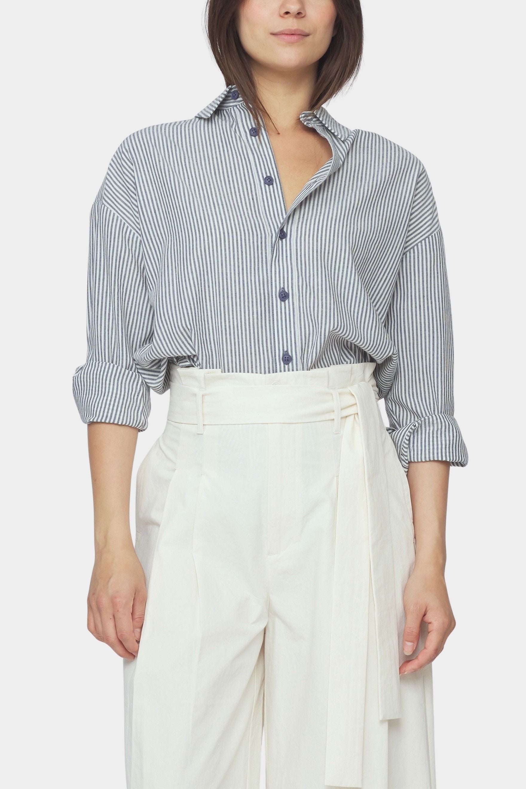 Close up front view of navy striped cotton dolman shirt with rolled sleeves and button placket tucked into ivory trousers