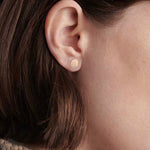 Model wearing small gold disc stud earrings with textured organic finish.