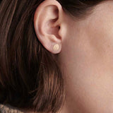 Model wearing small gold disc stud earrings with textured organic finish.