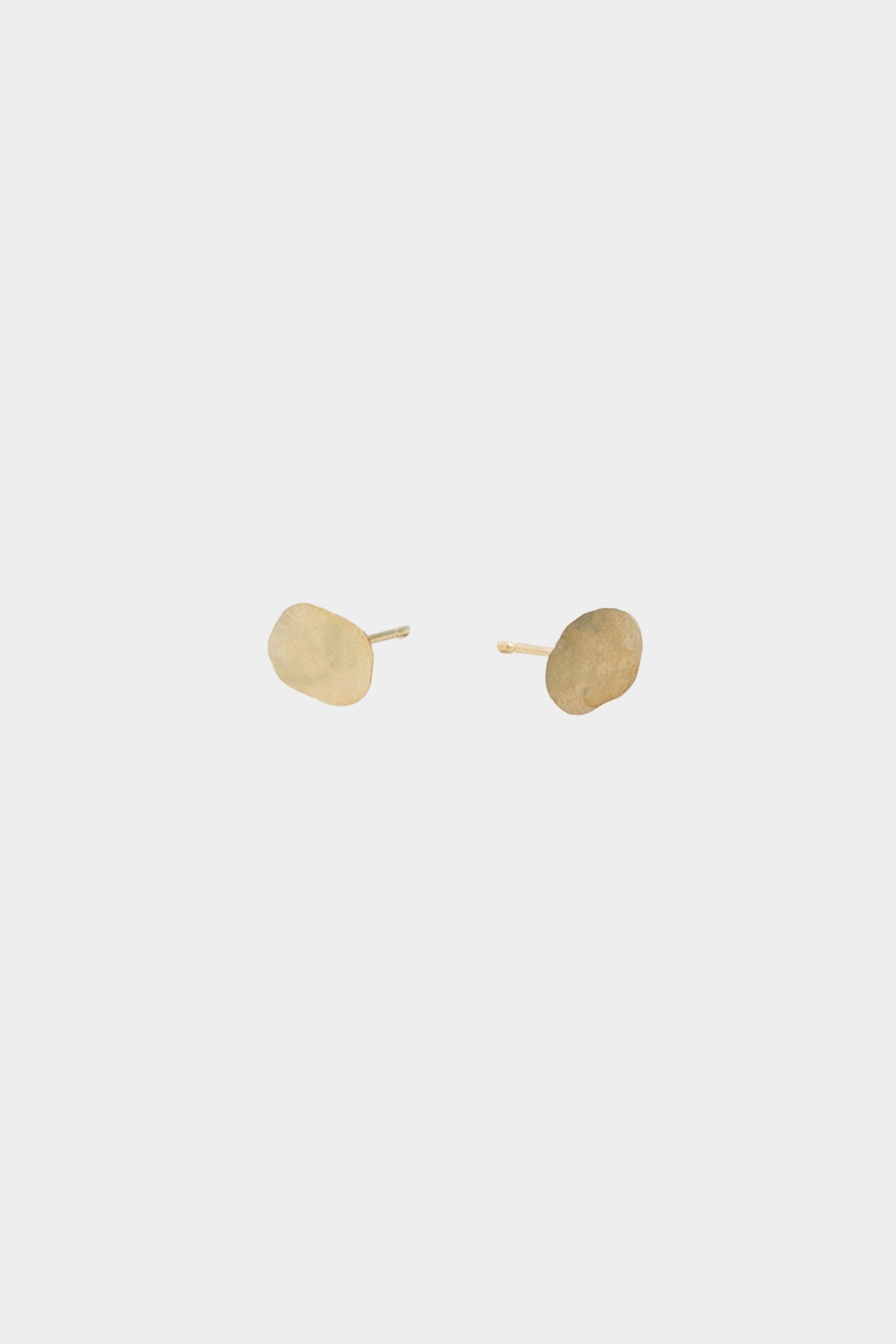 Minimalist gold disc stud earrings with organic shape on neutral background.
