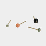 Minimalist gold stud earrings with multicolor gemstone accents on neutral background.