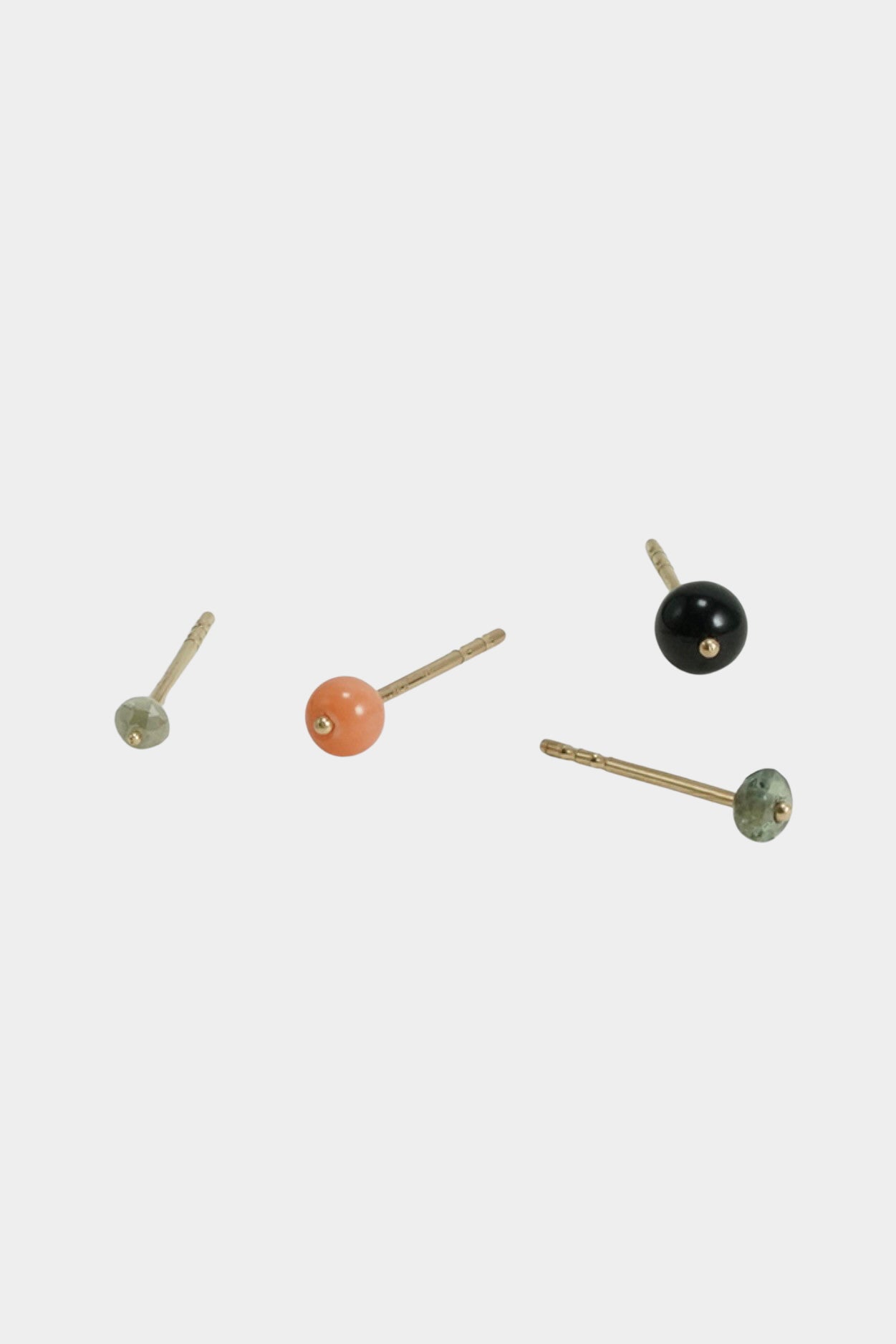 Minimalist gold stud earrings with multicolor gemstone accents on neutral background.