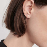 Model wearing small gold disc stud earrings with organic matte texture.