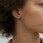Model wearing 14K gold minimalist bar stud earrings.