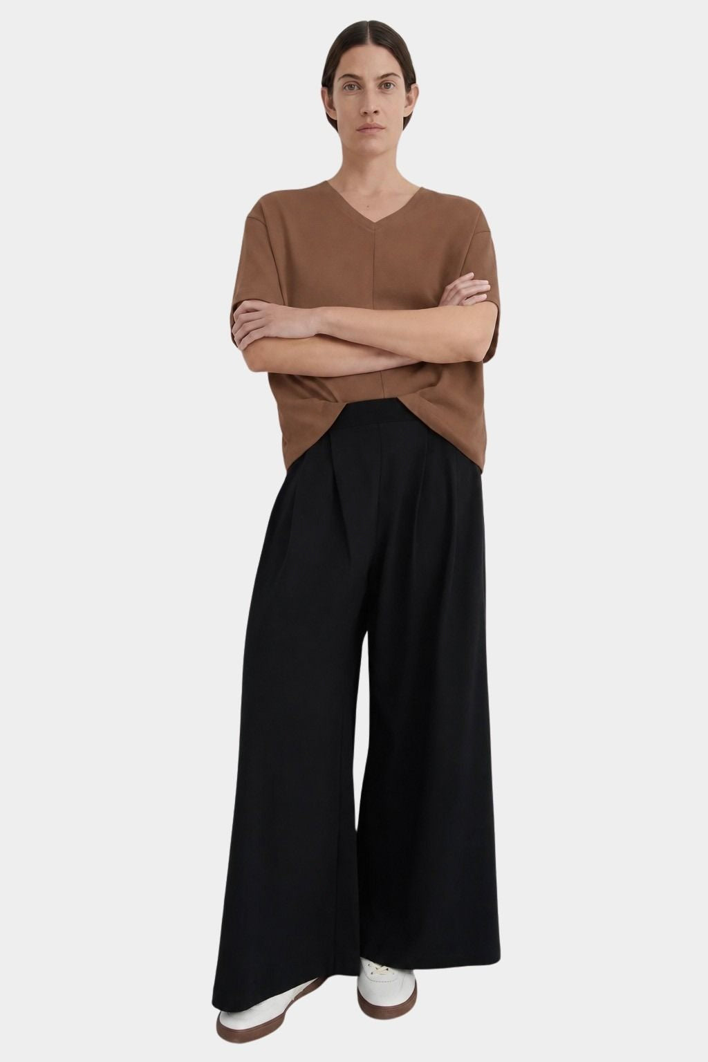 Front view of a model wearing the black Kowtow Drape Pant with a brown tee and white sneakers.