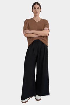 Front view of a model wearing the black Kowtow Drape Pant with a brown tee and white sneakers.