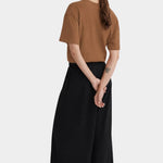 Back view of the black Kowtow Drape Pant worn with a brown tee and white sneakers at YUCCA Denver.