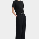 Three-quarter view of the black Kowtow Franz Pant with a black tee and red sandals.