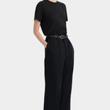 Three-quarter view of the black Kowtow Franz Pant with a black tee and red sandals.