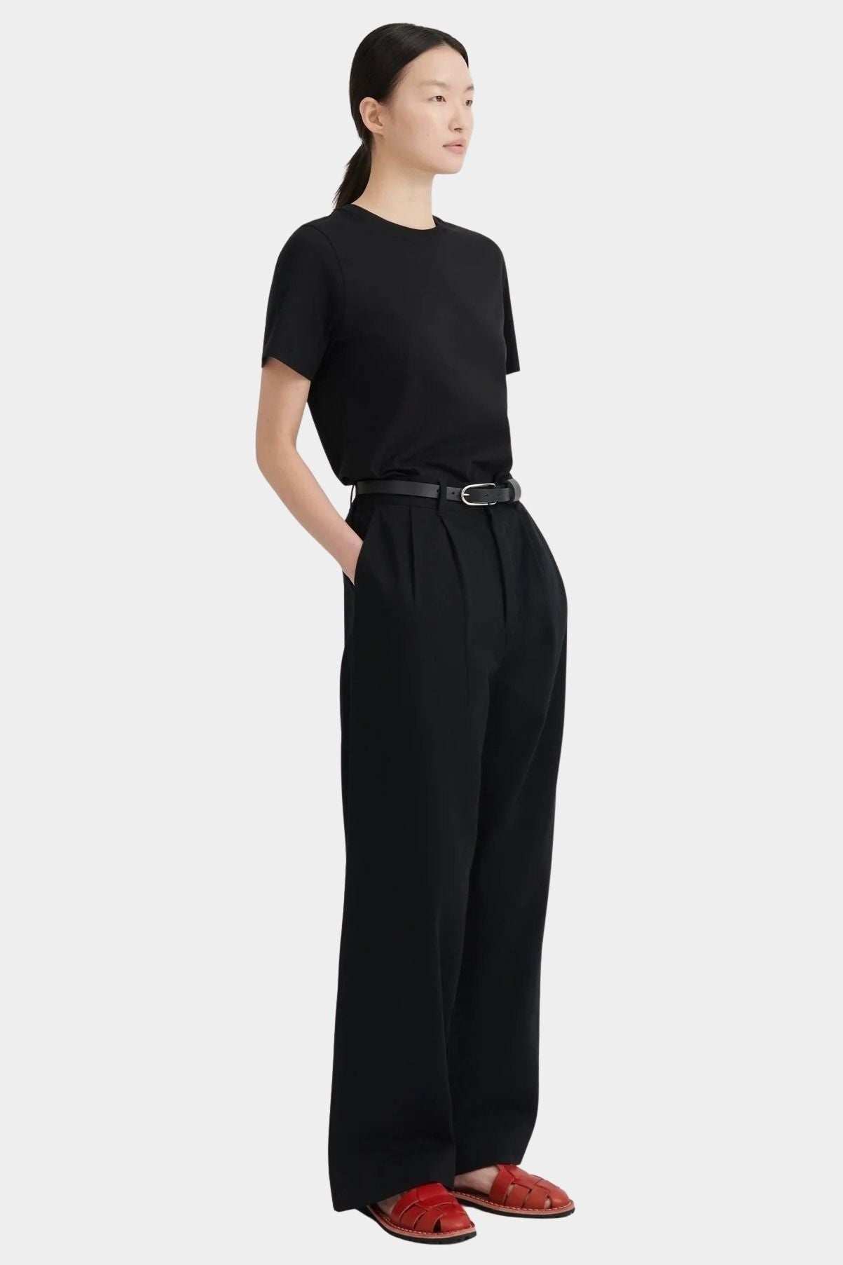 Three-quarter view of the black Kowtow Franz Pant with a black tee and red sandals.