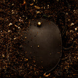 LINDQUIST Eggi bag in Chaga resting among soil and leaves, with pebbled leather and a spherical brass closure