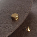 Close view of the Chaga Mezzo bag’s brass flap closure, pebbled leather, and tonal stitching