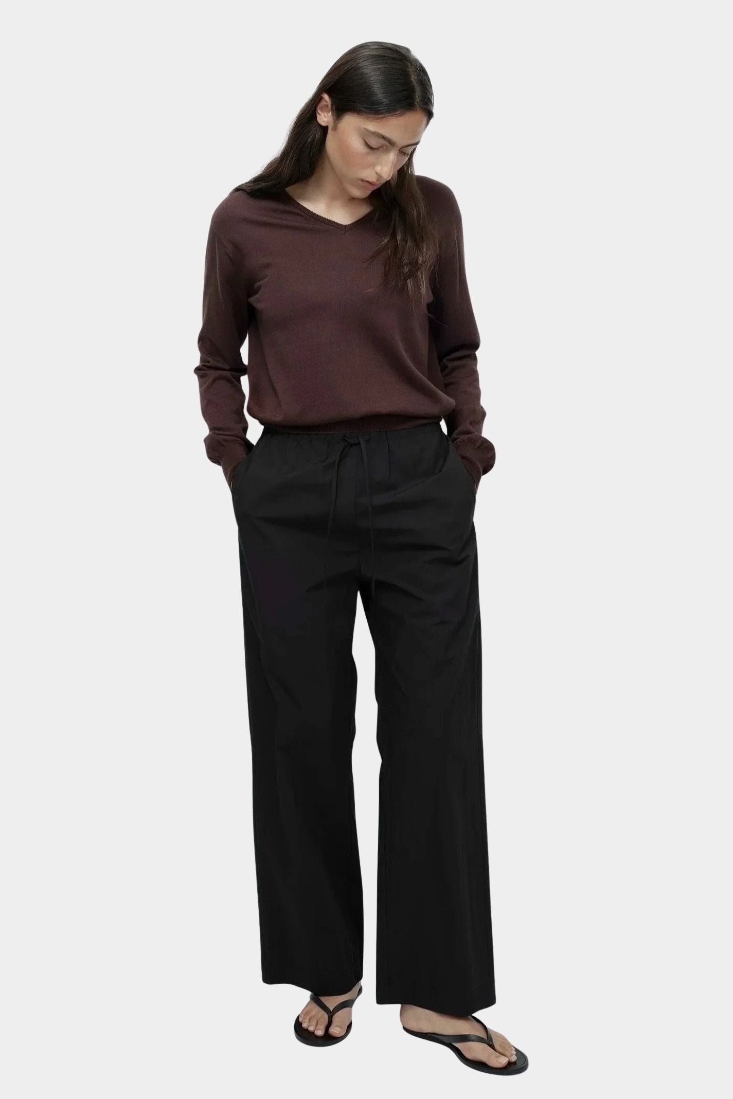 Full look of brown cotton blend v neck knit top by Mijeong Park with relaxed fit and black wide leg pants