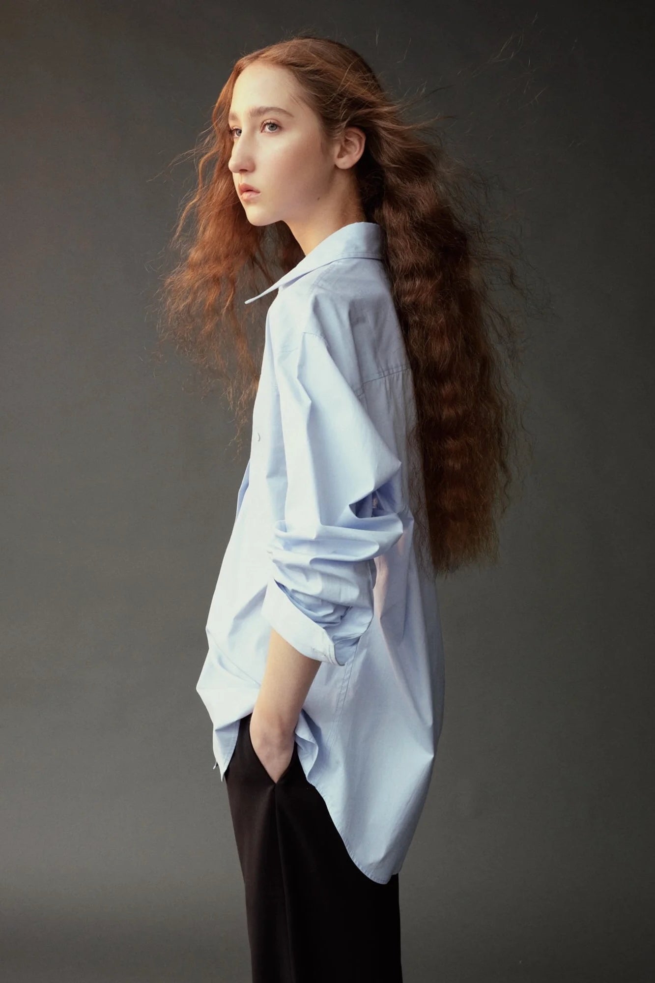 Side view of the Mijeong Park light blue oversized shirt styled with dark wide leg trousers