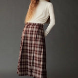 Model wearing the Mijeong Park brown plaid midi skirt with front pleats and an ivory turtleneck