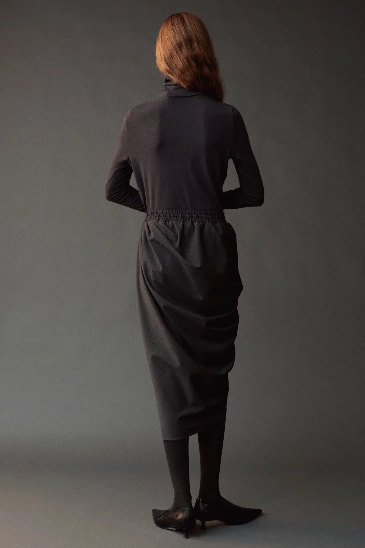 Graphite roll neck jersey top styled with a draped charcoal skirt and tights.