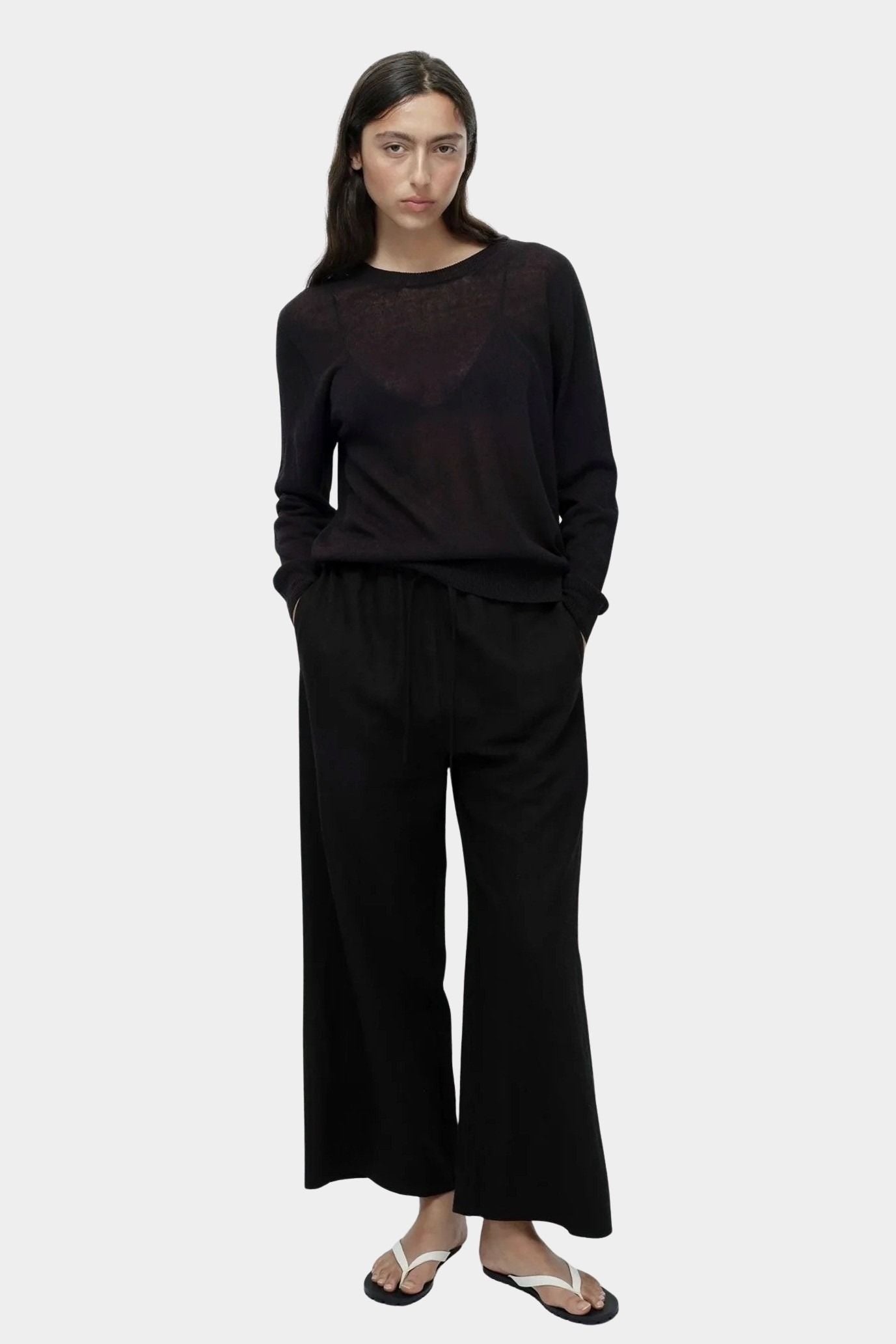 Front view of semi sheer linen blend knit top in black by Mijeong Park styled with wide leg black trousers