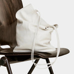 Modern Weaving Slim Elongated Tote Creme in Italian lamb leather draped over wooden chair with soft structure and long shoulder straps