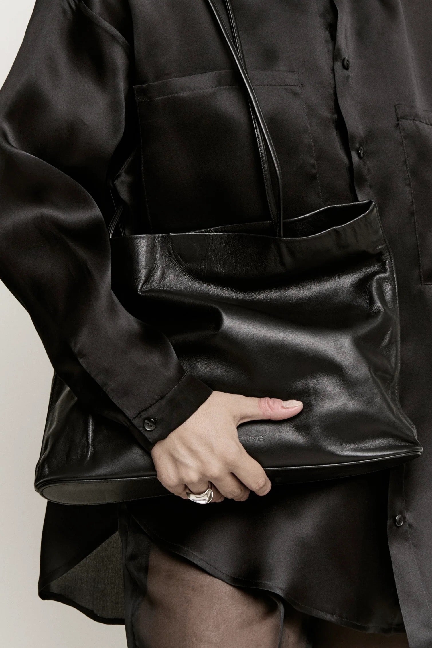 Modern Weaving Narrow Oval Relaxed Tote in black leather, soft slouchy shoulder bag with wide strap and minimal silhouette, styled with black silk shirt and tights
