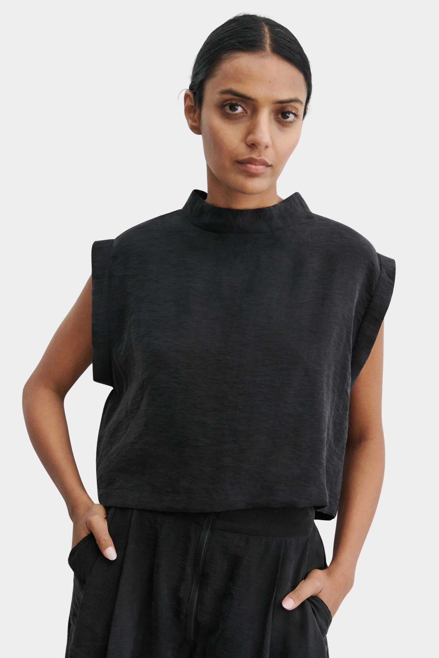 Rachel Comey Bacchus top in black with sculptural sleeveless design, structured mock neckline, and boxy cropped silhouette, styled with matching trousers